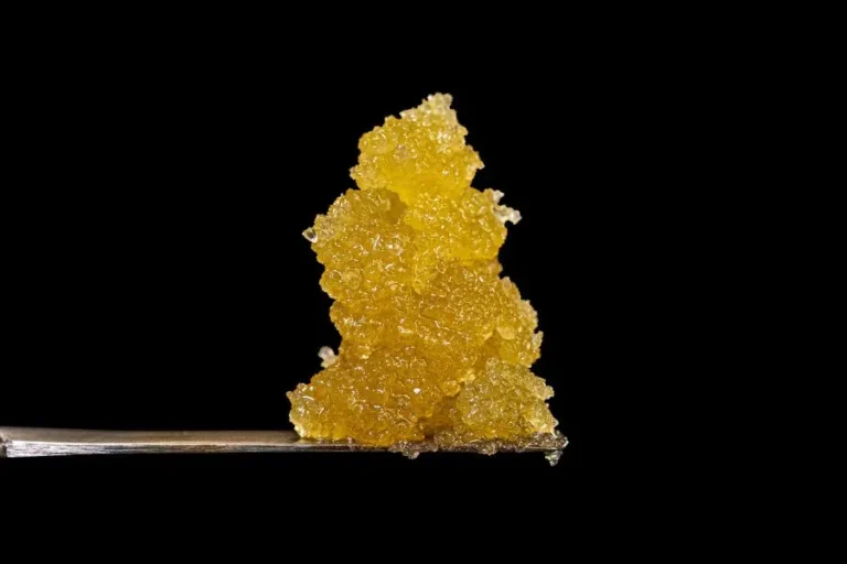 Close-up of golden cannabis concentrate (likely live resin or sugar wax) sitting on a dab tool against a black background