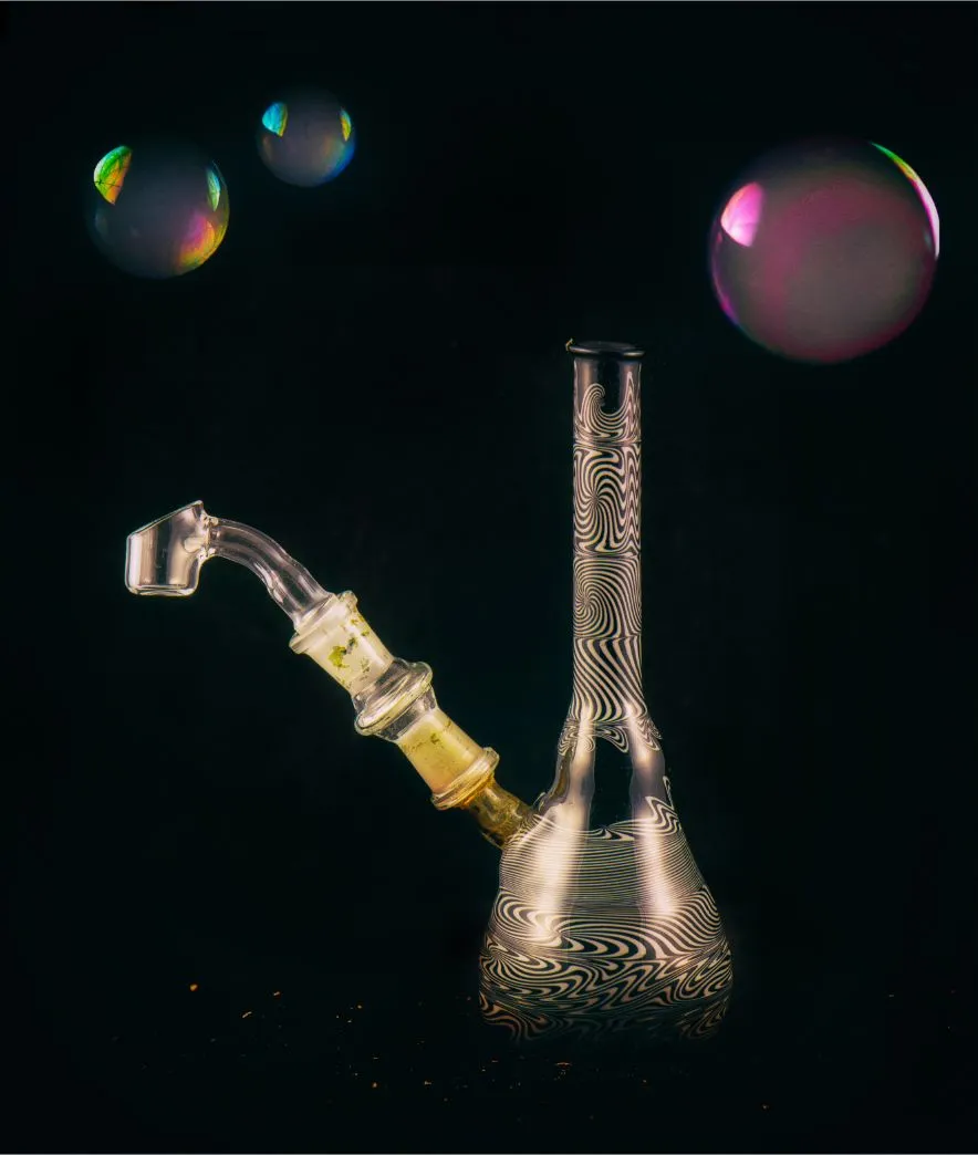 Artistic photo of a glass dab rig with colorful patterns, surrounded by floating bubbles, used for consuming cannabis concentrates
