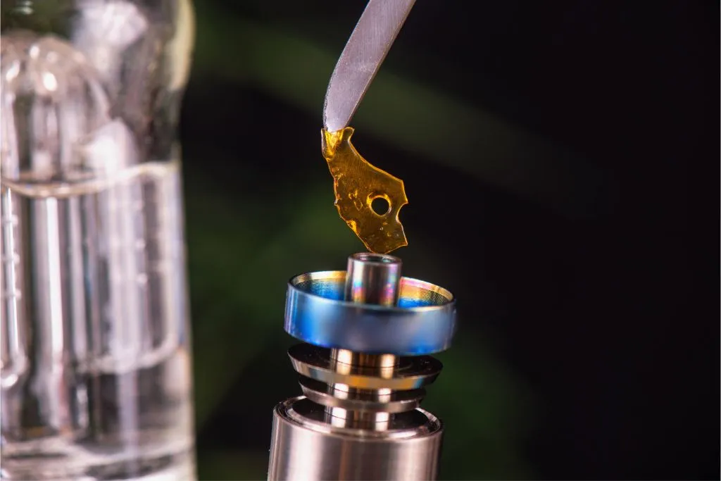 A dab tool holding amber cannabis concentrate over a heated nail on a dab rig, ready for dabbing