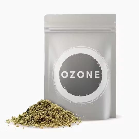 Silver resealable pouch labeled “Ozone” with a portion of ground cannabis flower displayed beside it. Product shown is the Blueberry Pie strain.