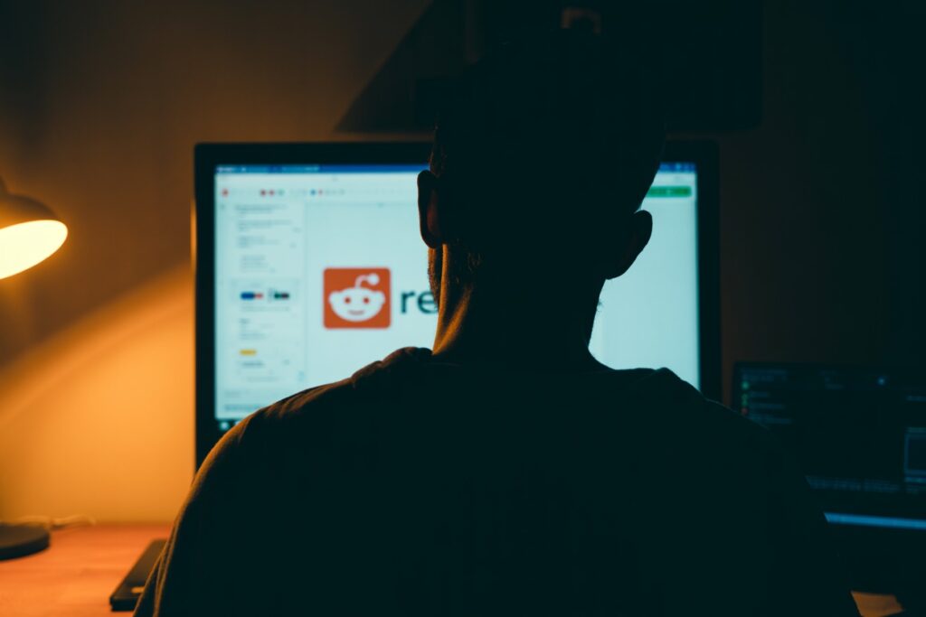 Silhouette of a man browsing Reddit on a desktop in a dark room – cannabis enthusiast researching top cannabis brands through Reddit communities and reviews.