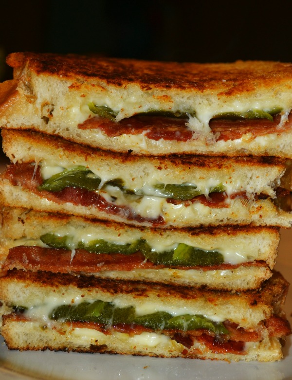A stack of sandwiches with bacon, jalapeno, and melted cheese filling