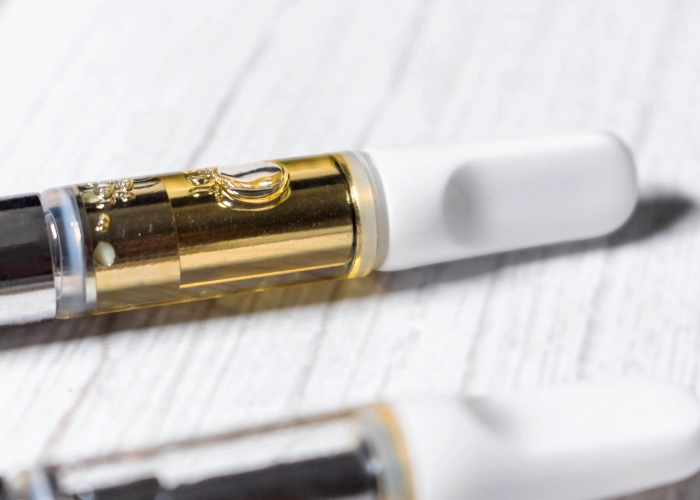Close-up of a cannabis vape cartridge with golden chamber and white mouthpiece on a light marble surface
